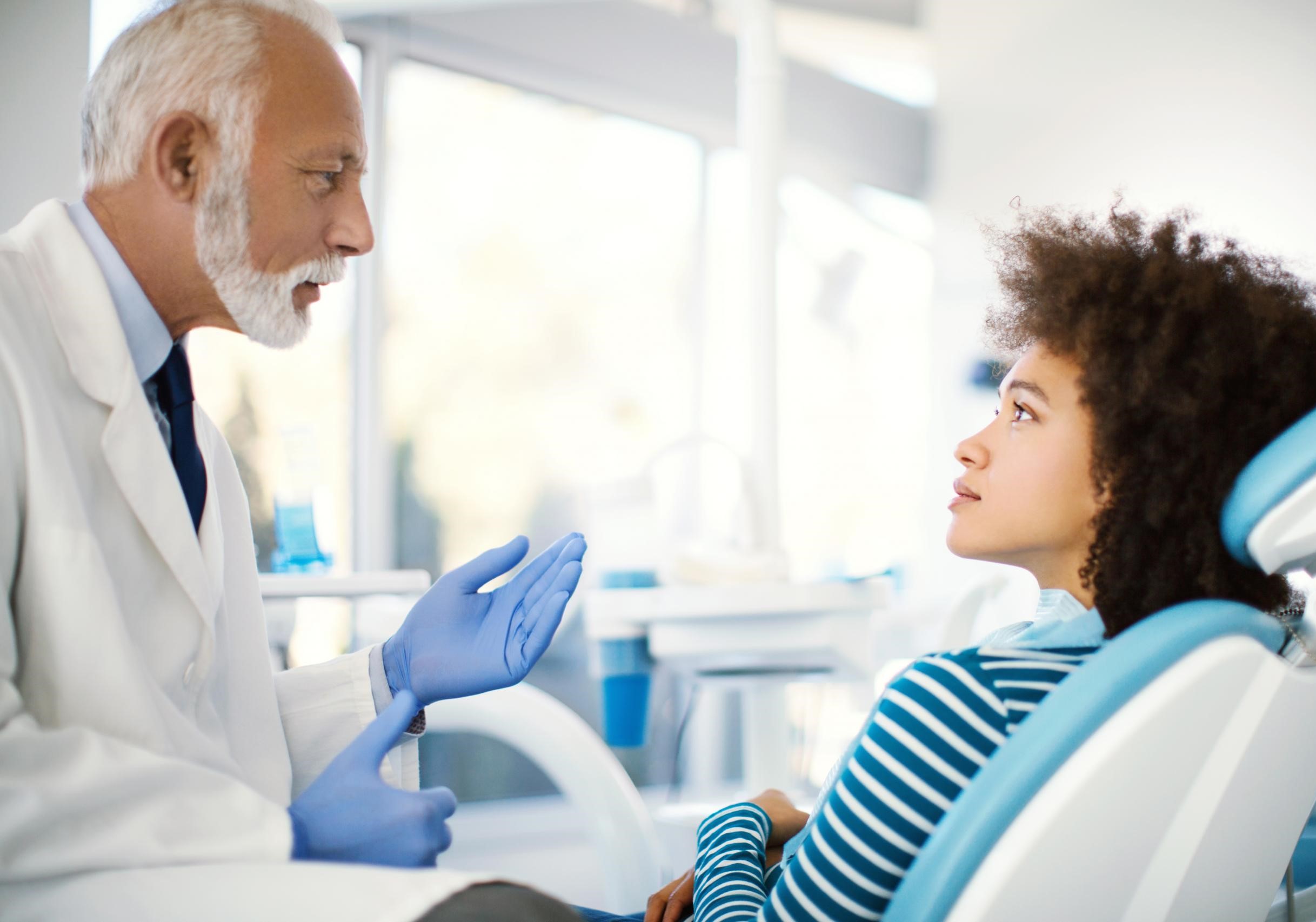 A patient in a dental chair being spoken to by their provider.