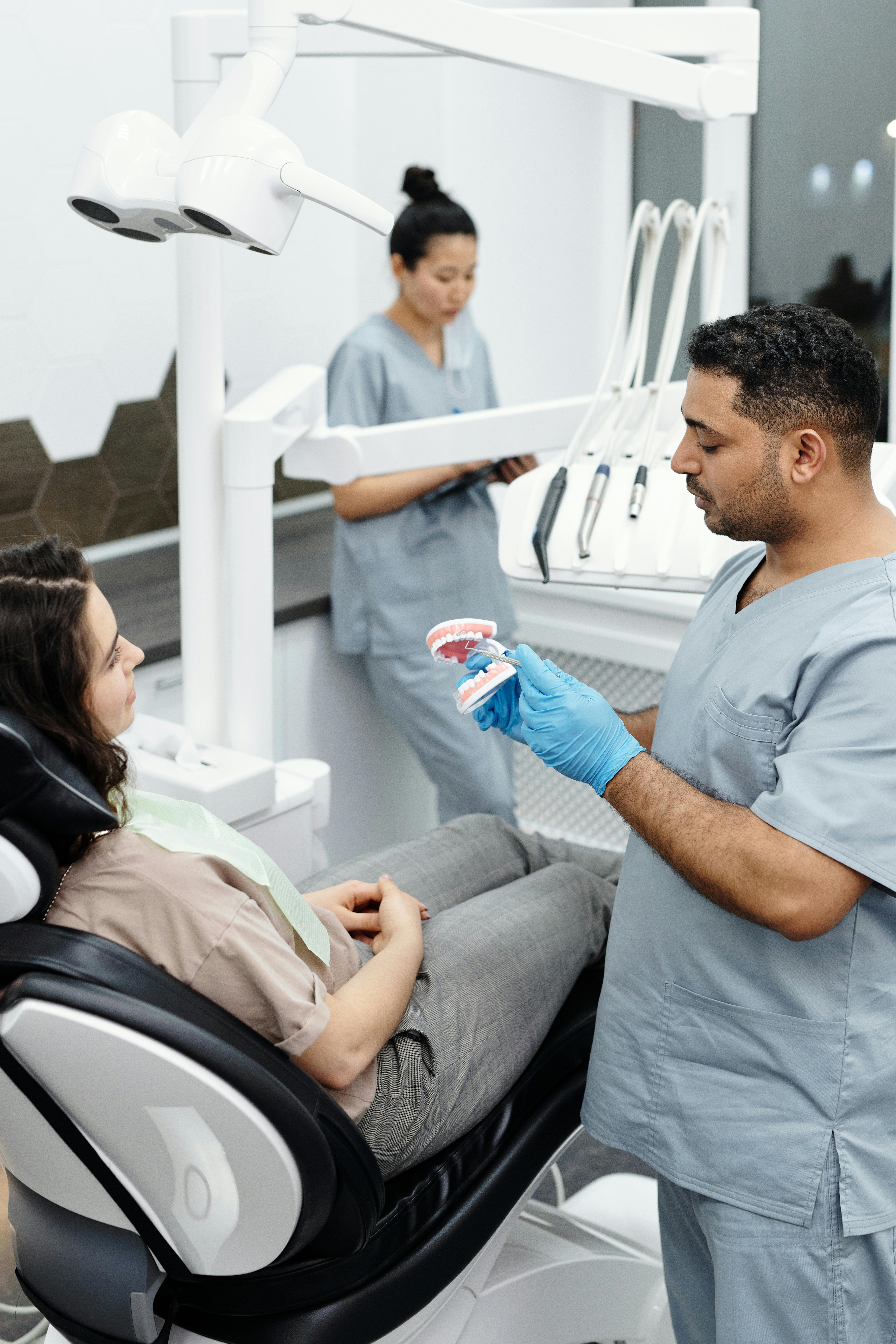 A patient in a dental chair being shown a model of teeth during a consultation.